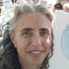A woman with curly hair hods a hand drawn earth sign while at a climate protest